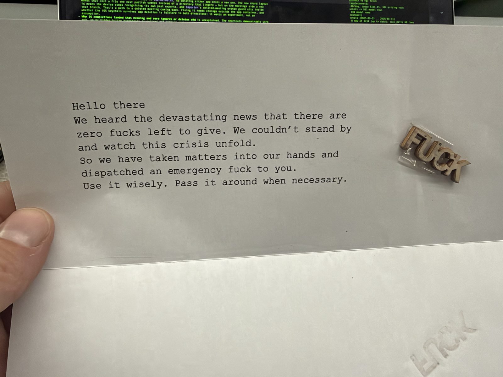 A typewritten letter reading 'We heard the devastating news that there are zero fucks left to give' beside a small laser-cut wooden piece spelling the word FUCK